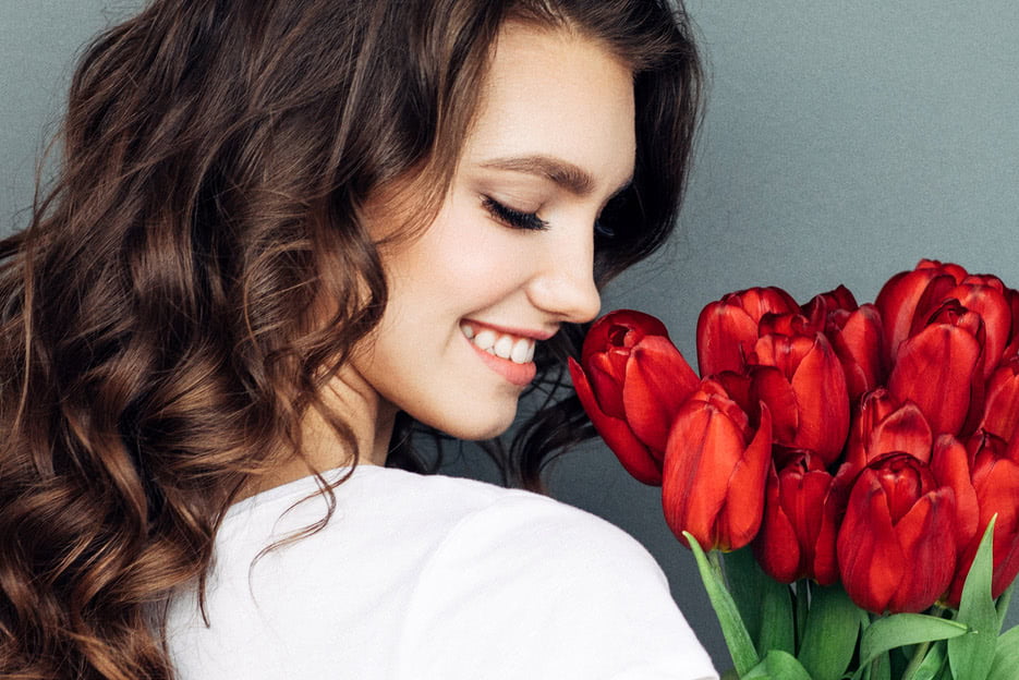 woman with beautiful skin smiling at bouquet of roses