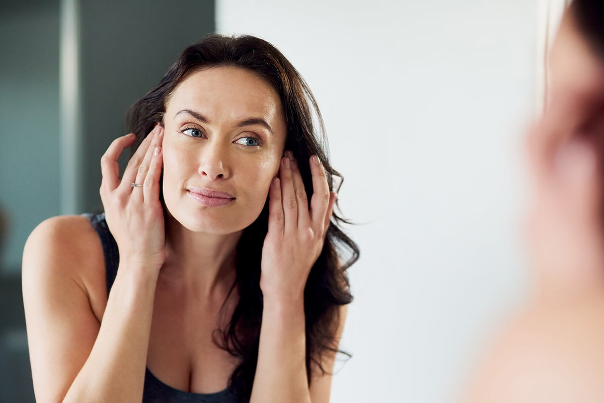 woman gazes at her naturally healthy skin in mirror