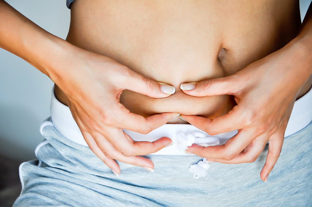 Woman in blue shorts pinches fat in belly