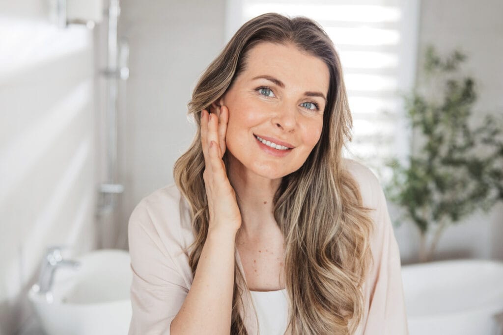 Mature woman in her early 40s touching skin in the mirror after full facial rejuvenation