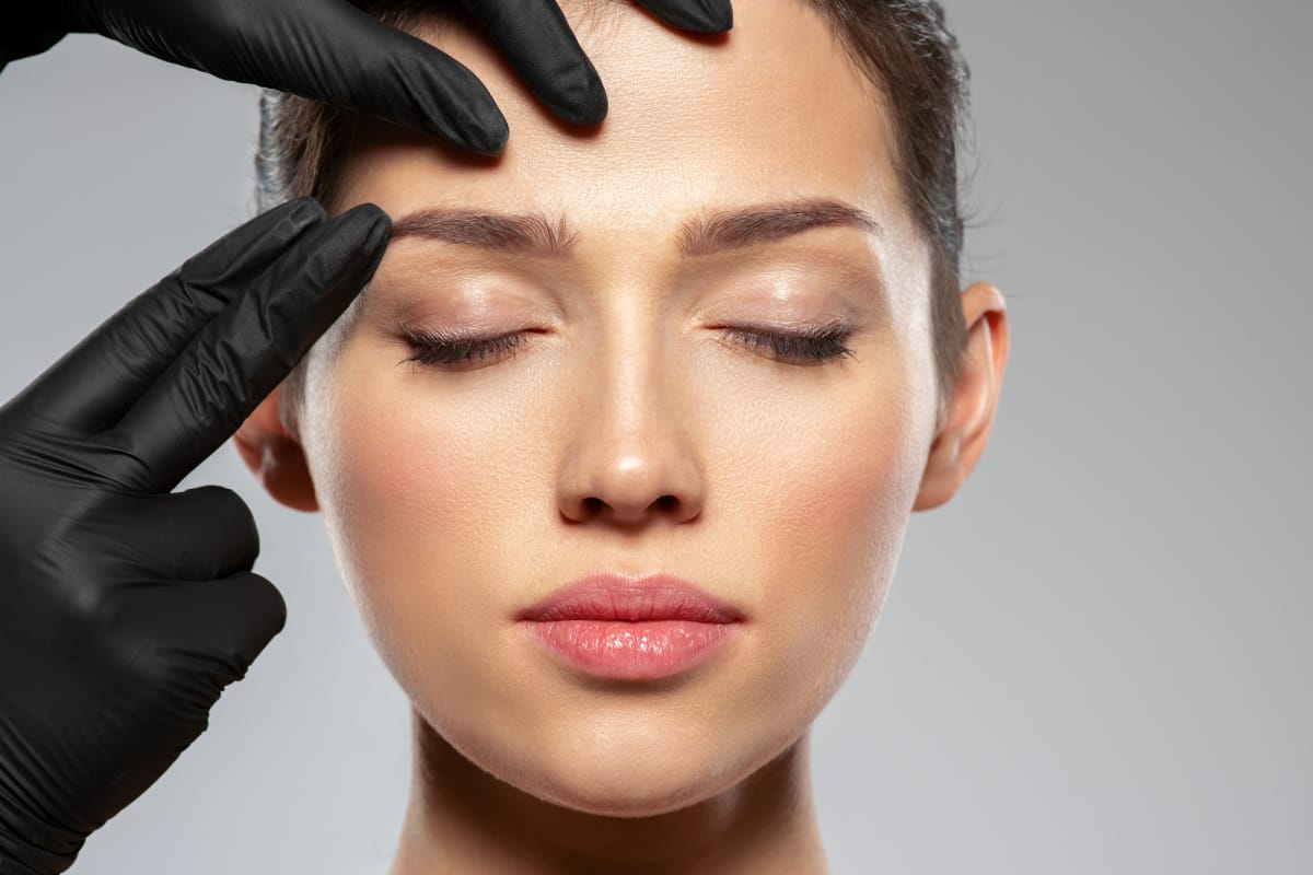 Aesthetician with black gloves checking patient's skin before Botox injections